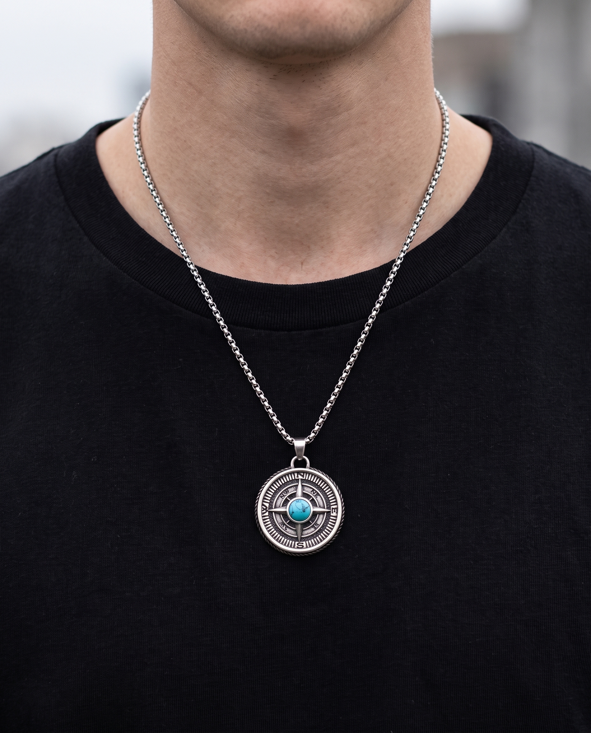 Man wearing a turquoise compass pendant necklace with a black T-shirt