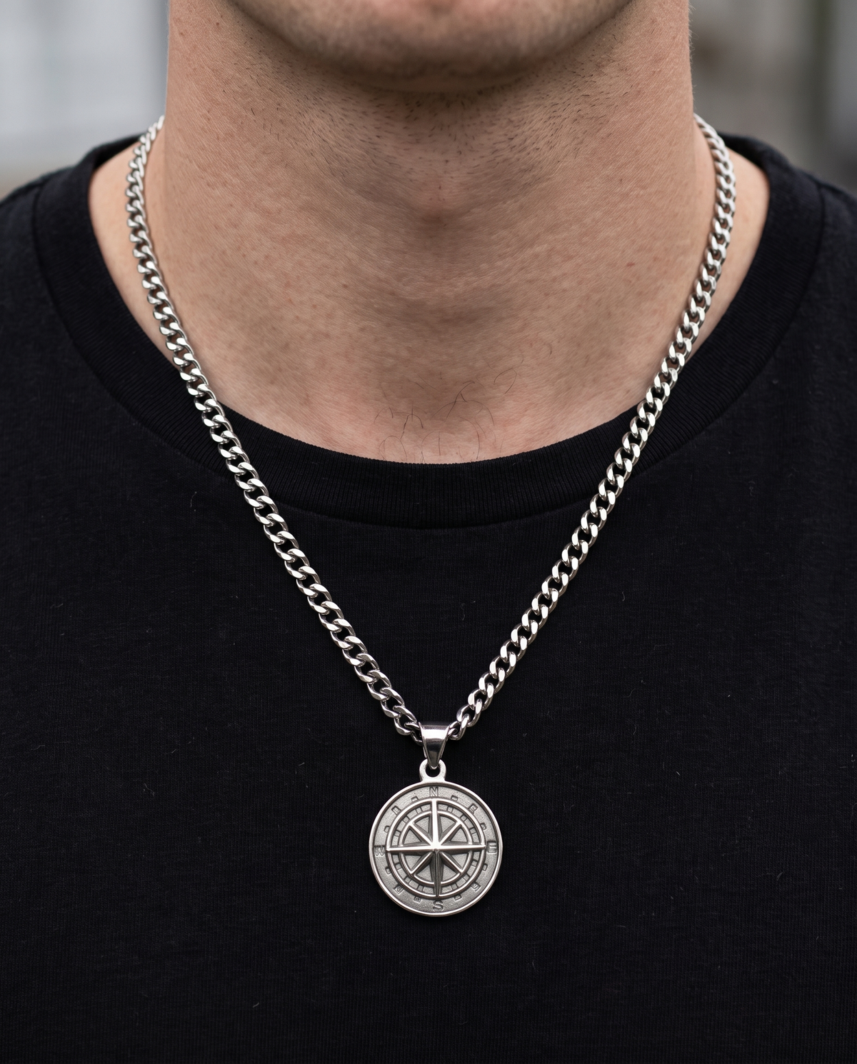 Man wearing a silver compass pendant necklace with a black T-shirt